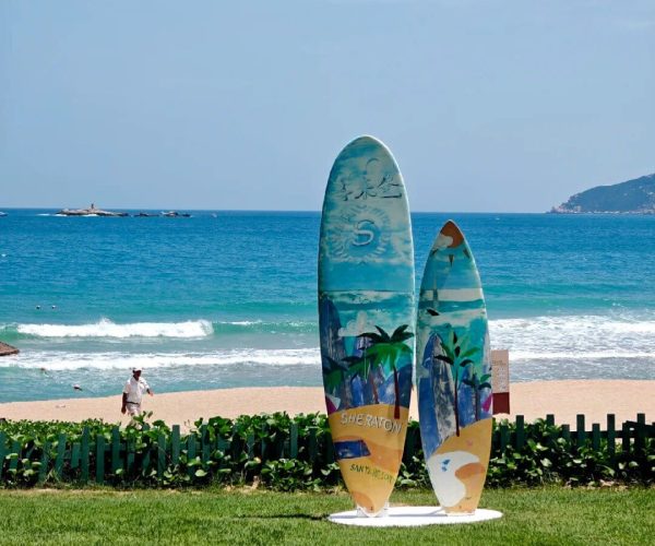Yalong Bay National Resort Area,Sanya,Chinatravel Two colorful surfboards planted upright on a green lawn beside a sandy beach and blue ocean.
