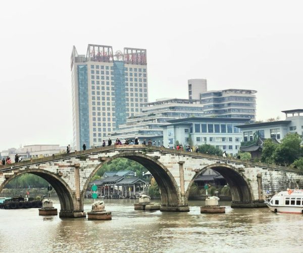 Grand Canal of China,Suzhou,Chinatravel Stone arched bridge over a river with pedestrians, modern buildings in the background says city skyline