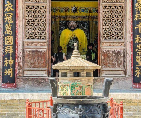 Fuxi Temple,Tianshui,China tour Temple doorway with gold Chinese characters and a large yellow-robed statue visible inside; a decorative incense burner sits in the foreground.