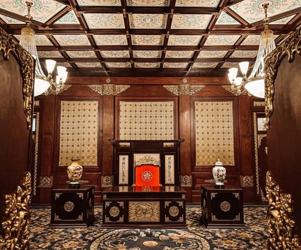 Museum of the Imperial Palace of the Manchu State,Changchun,China tour Ornate antique Asian-style ceremonial room with dark wood panels, gold accents, and a central red-throne chair with decorative vases nearby.