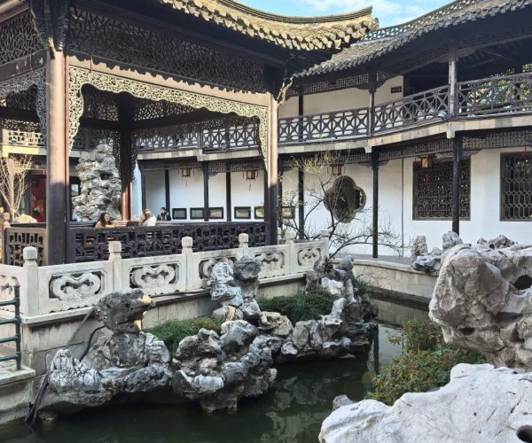 Traditional Chinese garden pavilion with carved wooden lattice, rocks, and a reflecting pond.