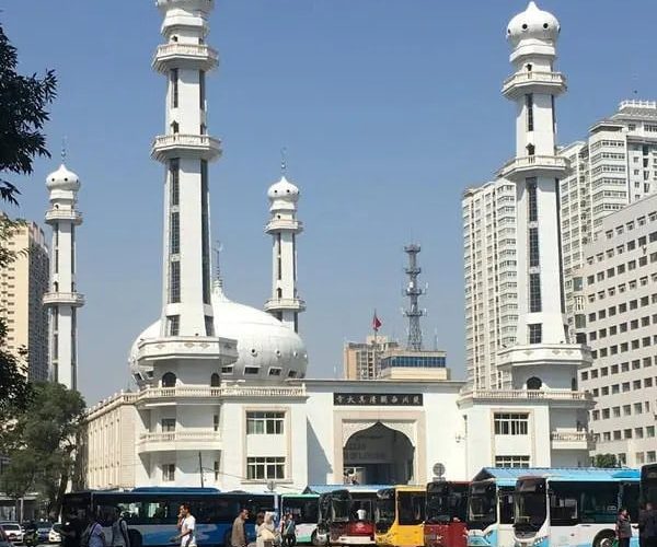 Xiguan Mosque,Lanzhou,China tour White mosque with four tall minarets and a central dome in a busy city street; buses and pedestrians in front.