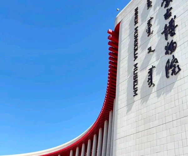 Inner Mongolia Museum,Hohhot,Chinatrip Exterior of a modern museum with tall white walls, red curved supports, and vertical Chinese lettering against a blue sky.