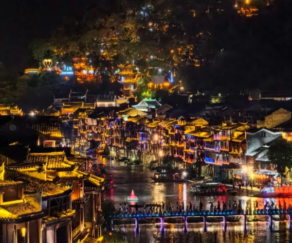 Fenghuang Ancient Town,Fenghuang,Chinatravel Nighttime riverside town with lantern-lit buildings, a crowded promenade, and reflections on the water.