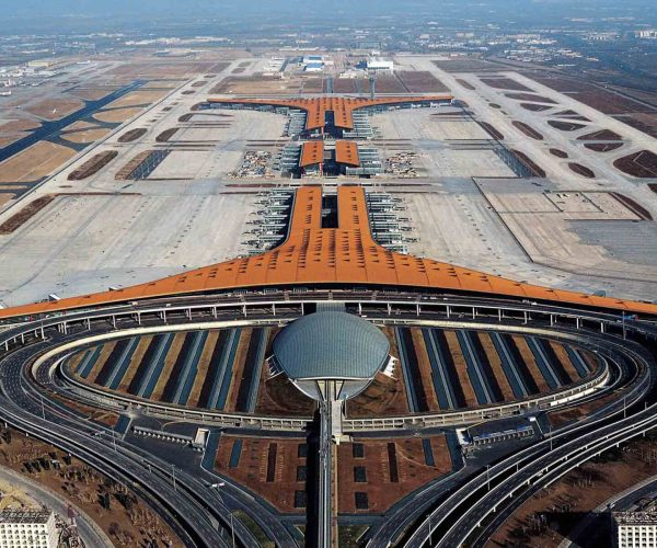 Beijing Capital International Airport, beijing, chinatravel, Aerial view of a large airport terminal with an orange roof and a central spine, surrounded by circular roadways and concourses.