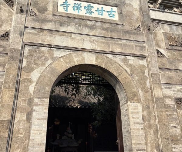 Beigu Hill/Temple,Zhenjiang,China tour Stone temple gate with a blue-panel inscription above an arched doorway, and a red Buddhist character 佛 at the top, opening to a courtyard with ritual vessels inside.