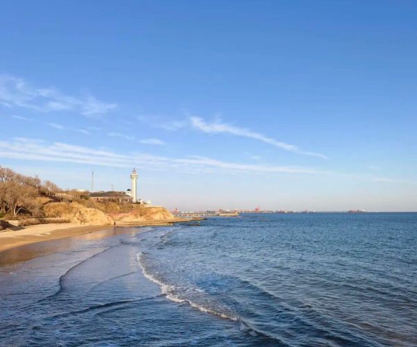 Beidaihe Seaside Resort,Qinhuangdao,Chinatravel Coastal scene with a sandy beach, rocky shoreline, and a lighthouse on the cliff to the left under a clear blue sky