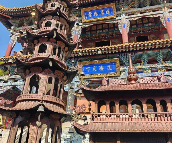 Tulou Temple Tibetan Buddhist Sites,Xining,Chinatrip Intricately carved multi-tier pagoda in front of a colorful traditional Chinese temple with blue plaques and ornate roofs under a clear sky.