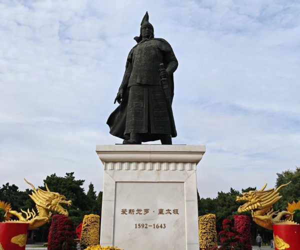 Beiling Park & Zhaoling Tomb,Shenyang,China tour Bronze statue of an armored warrior standing atop a marble pedestal, with gold dragon sculptures and colorful flower pots around it.