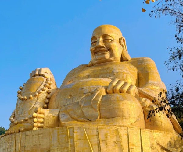 Thousand Buddha Mountain,Jinan,China tour Massive golden Buddha statue seated outdoors against a bright blue sky, holding a string of prayer beads in one hand.