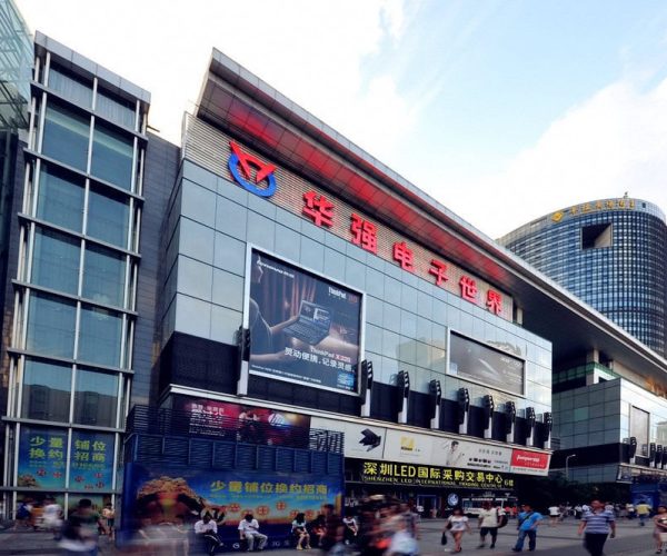 Huaqiangbei Electronics Market,Shenzhen,Chinatravel Exterior of a large modern shopping center with glass walls, big LED screens, and crowds in front.