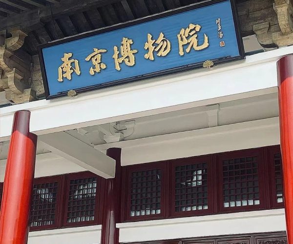 Nanjing Museum,Nanjing,China tour Blue plaque with gold Chinese characters reading 'Nanjing Museum' above the entrance of a traditional Chinese building with red pillars and decorative lattice doors.