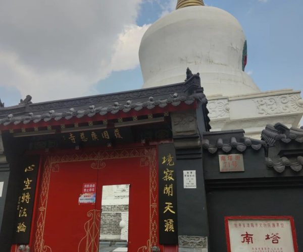 South Pagoda Monastery,Shenyang,China tour Traditional Chinese temple entrance with red doors, black and gold decorative panels, and a white stupa rising behind, under a cloudy sky