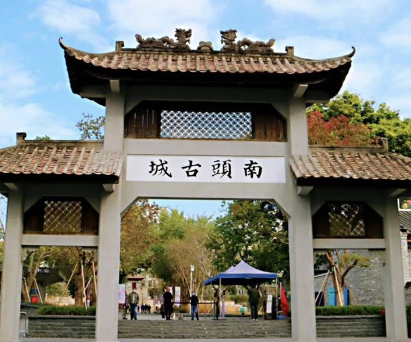 Nantou Ancient City,Shenzhen,Chinatravel Traditional Chinese-style gateway with a tiled, up-curved roof and decorative dragons on top, opening to a courtyard and trees; sign displays four Chinese characters above the entrance (the gate to Nan Tou Ancient Town).