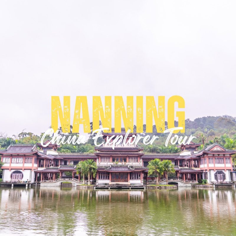 Nanning,Guangxi,Chinatravel Traditional Chinese-style building complex on a calm lake with trees and hills in the background, overlaid by large yellow 'NANNING' and white script text 'China Explorer Tour'.