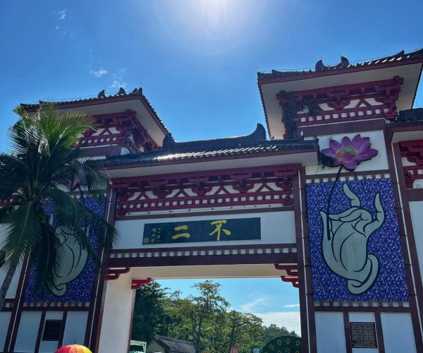 Nanshan Cultural Tourism Zone,Sanya,Chinatravel People walk through a Chinese-style gate with red beams and decorative lattice under a bright blue sky, flanked by lotus and hand murals on banners.