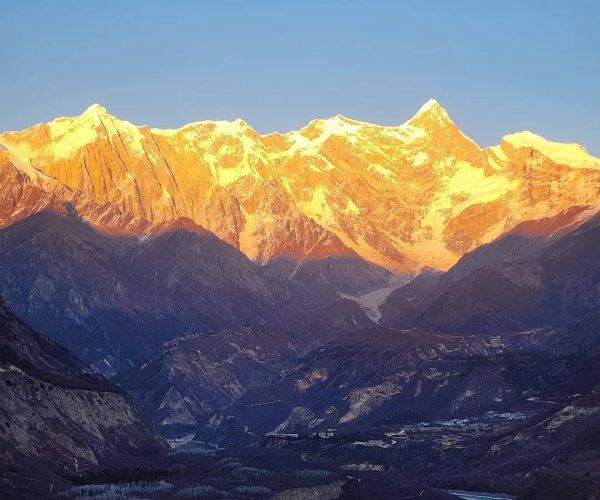 Nanga Parbat,Nyingchi,China tour Sunlit snow-capped mountains above a rocky valley with a winding river at dusk.