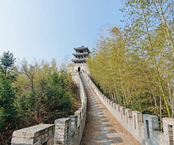 Southern Great Wall Ruins,Fenghuang,Chinatravel Stone walkway with brick railings winding uphill to a multi-tier pavilion surrounded by trees under a blue sky; a historic tower at the summit.