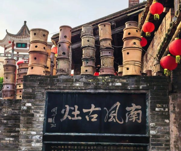 Nanfeng Kiln,Foshan,Chinatravel Entrance to a historic Chinese street with tall stacks of bamboo steamers on a brick wall and red lanterns hanging nearby.