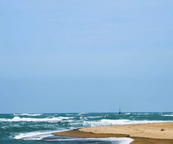 Bo’ao Jade Belt Beach,Qionghai,Chinatravel Calm sea with a sandy spit extending into the water and a distant navigational beacon on the horizon.