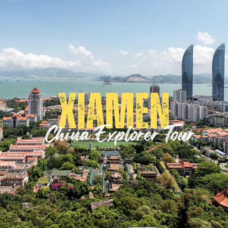 Xiamen,Fujina,Chinatravel Aerial view of Xiamen city with coast, skyscrapers and red-tiled roofs, overlaid with bold yellow ‘XIAMEN’ and white ‘China Explorer Tour’ text.”
