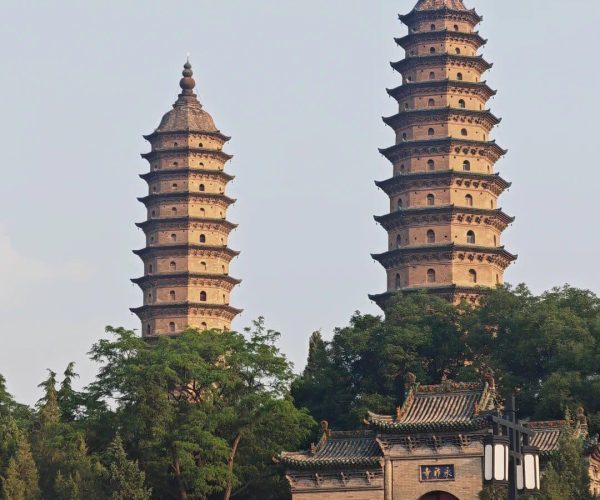 Shuangta Temple,Taiyuan,Chinatravel Two tall multi-tiered pagodas rise behind trees at a Chinese temple complex, with a gate and tiled courtyard in the foreground.