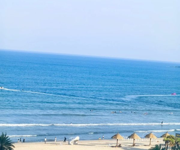 Shuangyue Bay,Huizhou,Chinatravel Beach scene with blue ocean, sandy shore, and striped straw umbrellas as people enjoy the water and coastline.