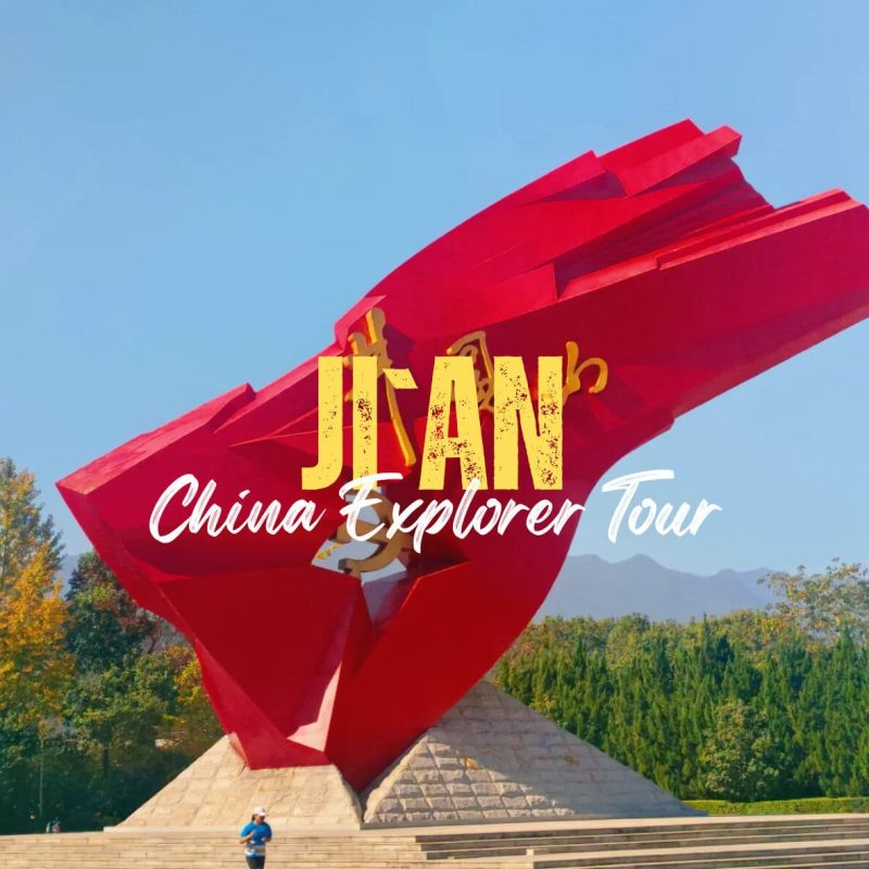 Ji'an,Jiangxi,China tour Red, abstract sculpture against a blue sky with trees in the background; overlaid text says 'JIAN China Explorer Tour'.