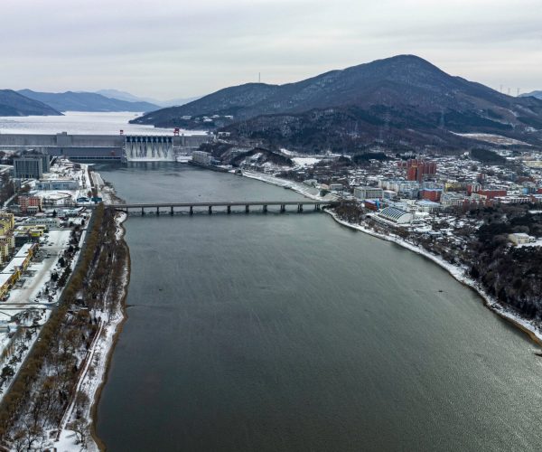 Jilin City,Jilin,Chinatrip Aerial winter view of a dam across a wide river with a town and hills in the background.