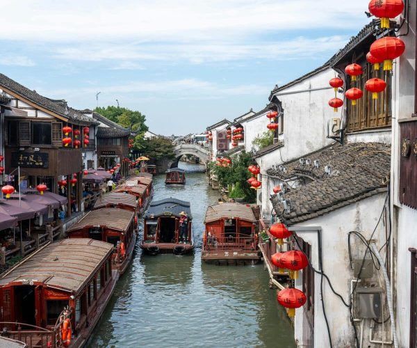 Zhouzhuang Water Town,Suzhou,Chinatravel Canal lined with wooden boats and white-walled buildings adorned with red lanterns in a traditional Chinese town setting.