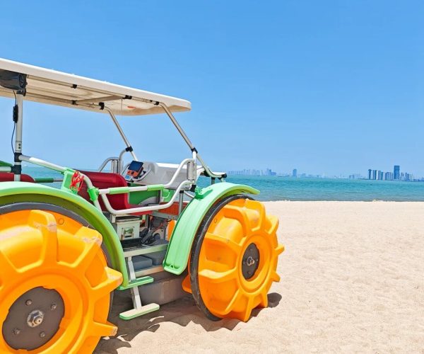 Holiday Beach,Haikou,Chinatravel Bright lime-green and orange beach tractor parked on sandy shore with calm blue water and distant city skyline in the background.