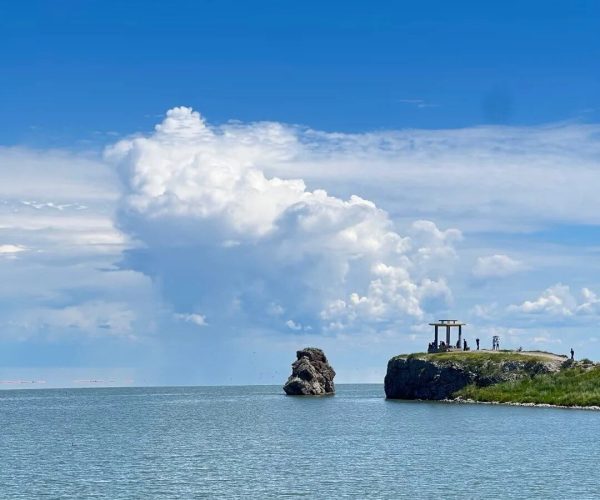 Hulun Lake,Manzhouli,China tour Cliffside viewpoint with a gazebo and several people overlooking calm blue water under a bright sky and large clouds