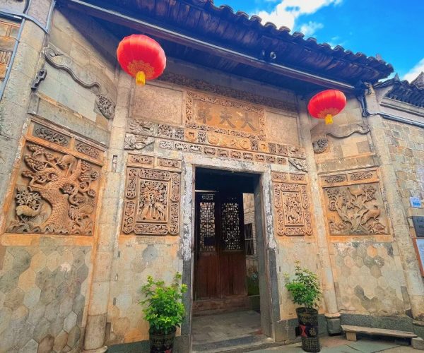 Hepingi Ancient Town,Nanping,Chinatravel Ornate carved stone doorway with detailed panels, two red lanterns hanging from the eaves, and a wooden door set in a historic brick wall; cobblestone path ahead.