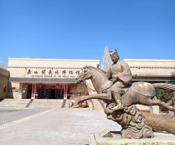 Great Wall Museum of Jiayuguan,Jiayuguan,China tour Statue of a man riding a rearing horse in front of the JiaYuguan Museum of the Great Wall, with the museum entrance and Chinese signage in the background under a clear blue sky.