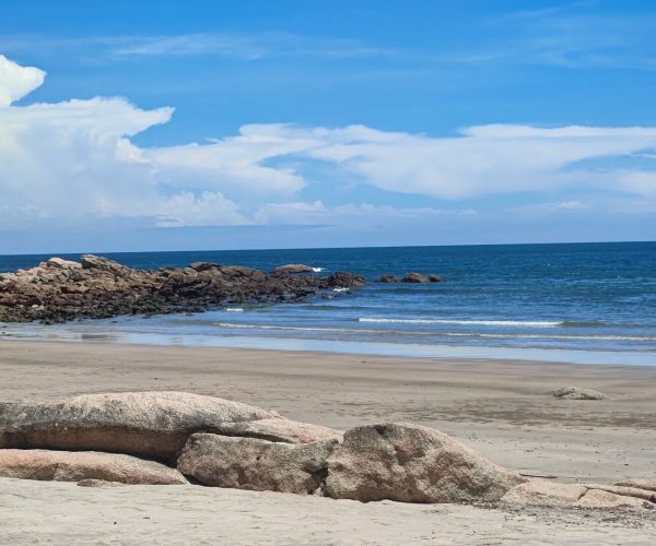 Zhuhai Islands (Wanshan, Dong’ao, Hebao),Zhuhai,Chinatravel Sunny beach scene with large rocks in the foreground, calm blue ocean and a clear sky with scattered clouds behind them.