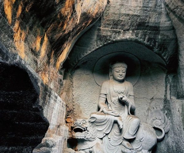 Great Buddha Temple,Shaoxing,Chinatravel Stone Buddha statue seated in a cave niche with a dragon at its base, carved from rock walls with warm light on the left edge.