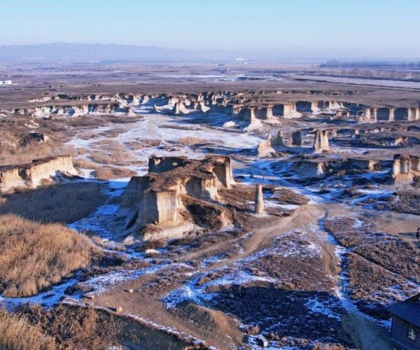 Datong Earth Forest,Datong,Chinatravel Wide view of a snow-dusted badlands landscape with eroded rock pillars under a clear blue sky.