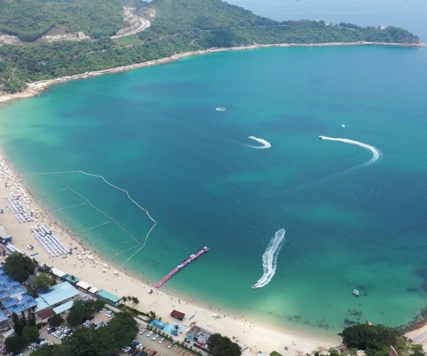 Dameisha & Xiaomeisha Beaches,Shenzhen,Chinatravel Aerial view of a turquoise bay with a sandy beach, sun loungers, and calm water encircled by green hills and buildings along the shore