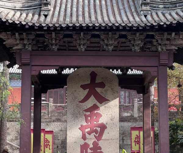Dayu Mausoleum Scenic Area,Shaoxing,Chinatravel Traditional Chinese temple gate with a curved tiled roof and a tall stone tablet inscribed with large red Chinese characters in a courtyard setting.