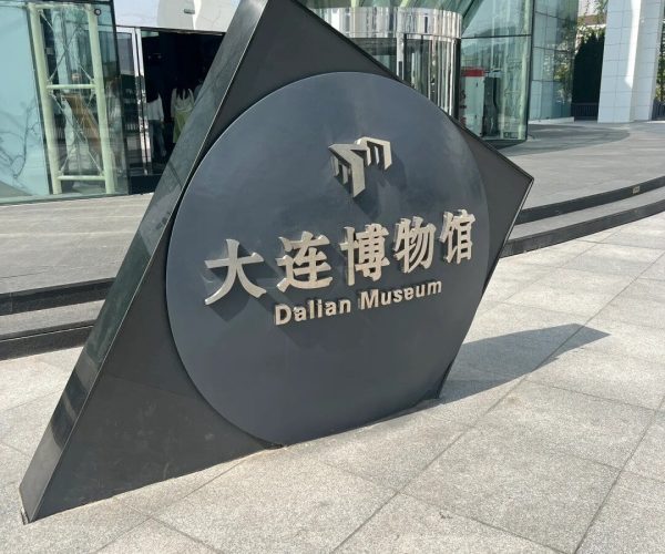 Dalian Modern Museum,Dalian,Chinatravel Modern plaza sign for Dalian Museum with Chinese characters and English 'Dalian Museum' in front of a glass atrium area.
