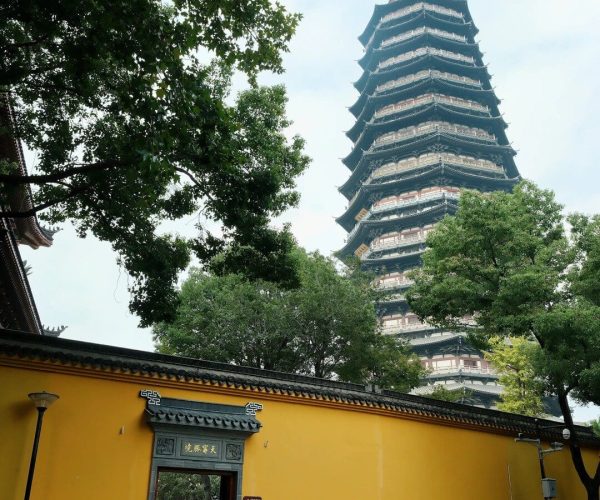 Tianning Temple,Changzhou,China tour Tall multi-tiered pagoda behind a yellow temple wall, with trees framing the scene.