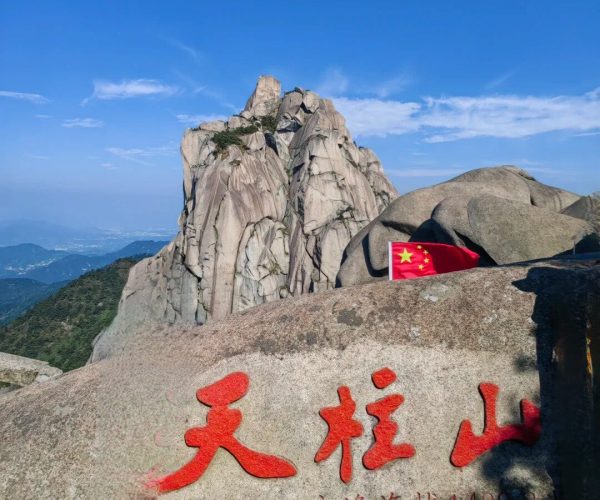 Tianzhu Mountain,Anqing,China tour Rugged granite peak under a clear blue sky; a small Chinese flag and red Chinese characters carved into a rock foreground a dramatic mountain landscape (Tianzhu Mountain).