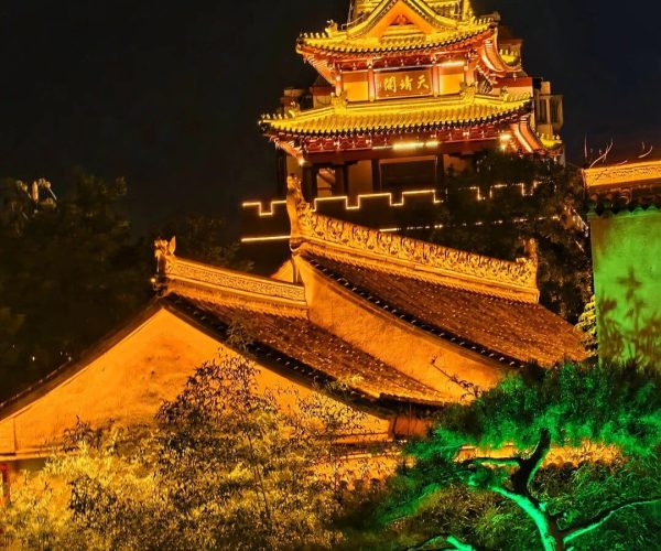 Tianshui Ancient City,Tianshui,China tour Night view of a multi-tier Chinese pagoda lit in warm gold, with ornate roofs and a surrounding garden.