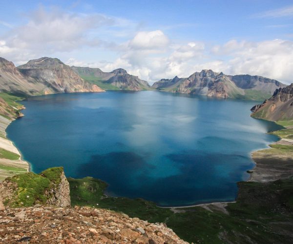 Changbai Mountain Heaven Lake,Baishan,Chinatrip Alpine lake in a valley, deep blue water bordered by rugged mountain peaks under a partly cloudy sky.