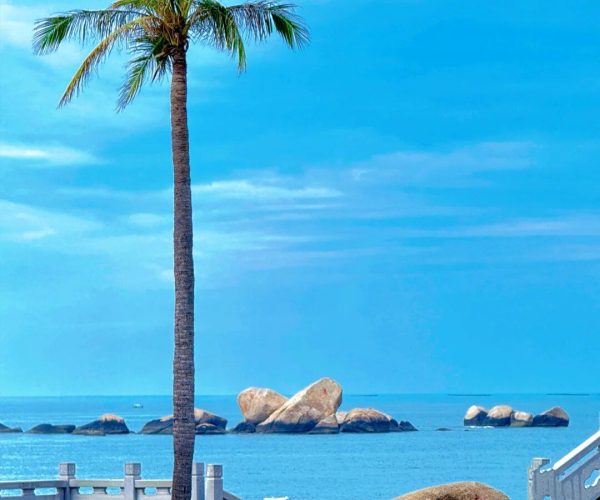 Tianya Haijiao,Sanya,Chinatravel Palm tree by a seaside promenade with a large rock carved in red Chinese character for love, overlooking calm blue water and distant rocks.