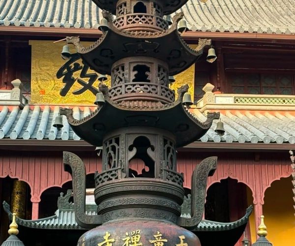 Tiantong Temple,Ningbo,Chinatravel Intricately carved bronze pagoda lantern in a temple courtyard, with golden Chinese characters on its base and a traditional tiled roof behind.