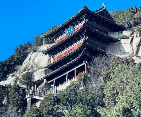 Tianlongshan Grottoes,Taiyuan,Chinatravel Three-story traditional Chinese pagoda perched on a rocky hillside under a bright blue sky, surrounded by trees.