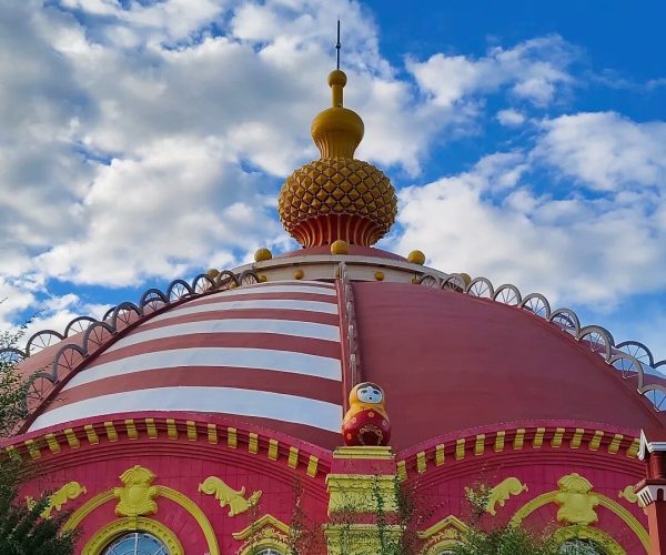 Manzhouli Matryoshka Square,Hulunbuir,Chinatrip Colorful domed building with pink and yellow façade and a gold onion dome against a blue sky.