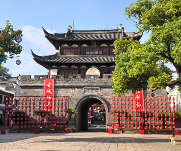 Wuzhou Ancient City,Zhejiang,Chinatravel Traditional Chinese gate and watchtower-style building atop a stone arch, flanked by rows of red lanterns and festival banners; blue sky and green trees in the background.