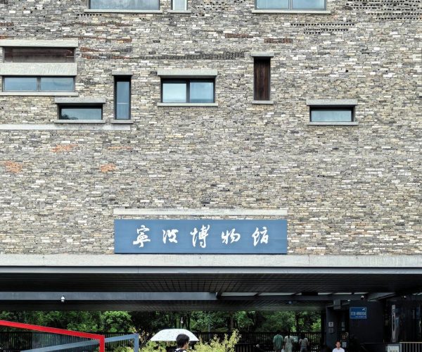 Ningbo Museum,Ningbo,Chinatravel Brick museum facade with a blue sign displaying Chinese characters, pedestrians outside under a covered entrance.